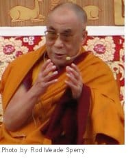 Dalai Lama. He is wearing orange robes and speaking into a microphone.
