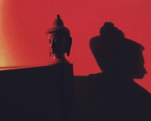 Image of a buddha head sculpture casting shadow on red wall.