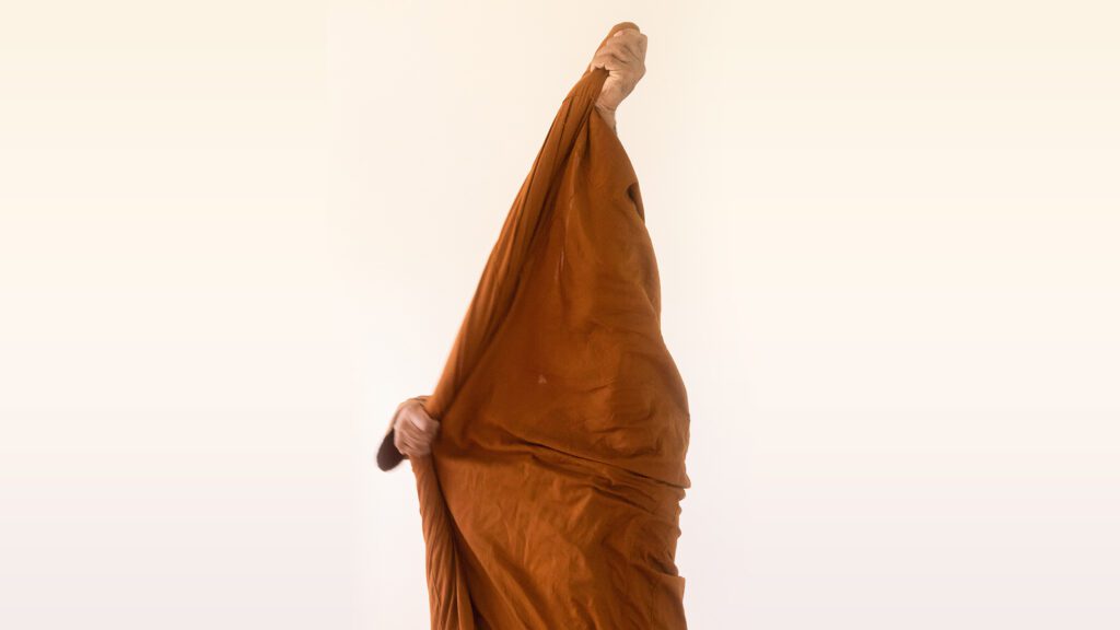 A Buddhist monastic holds up their saffron-colored robe