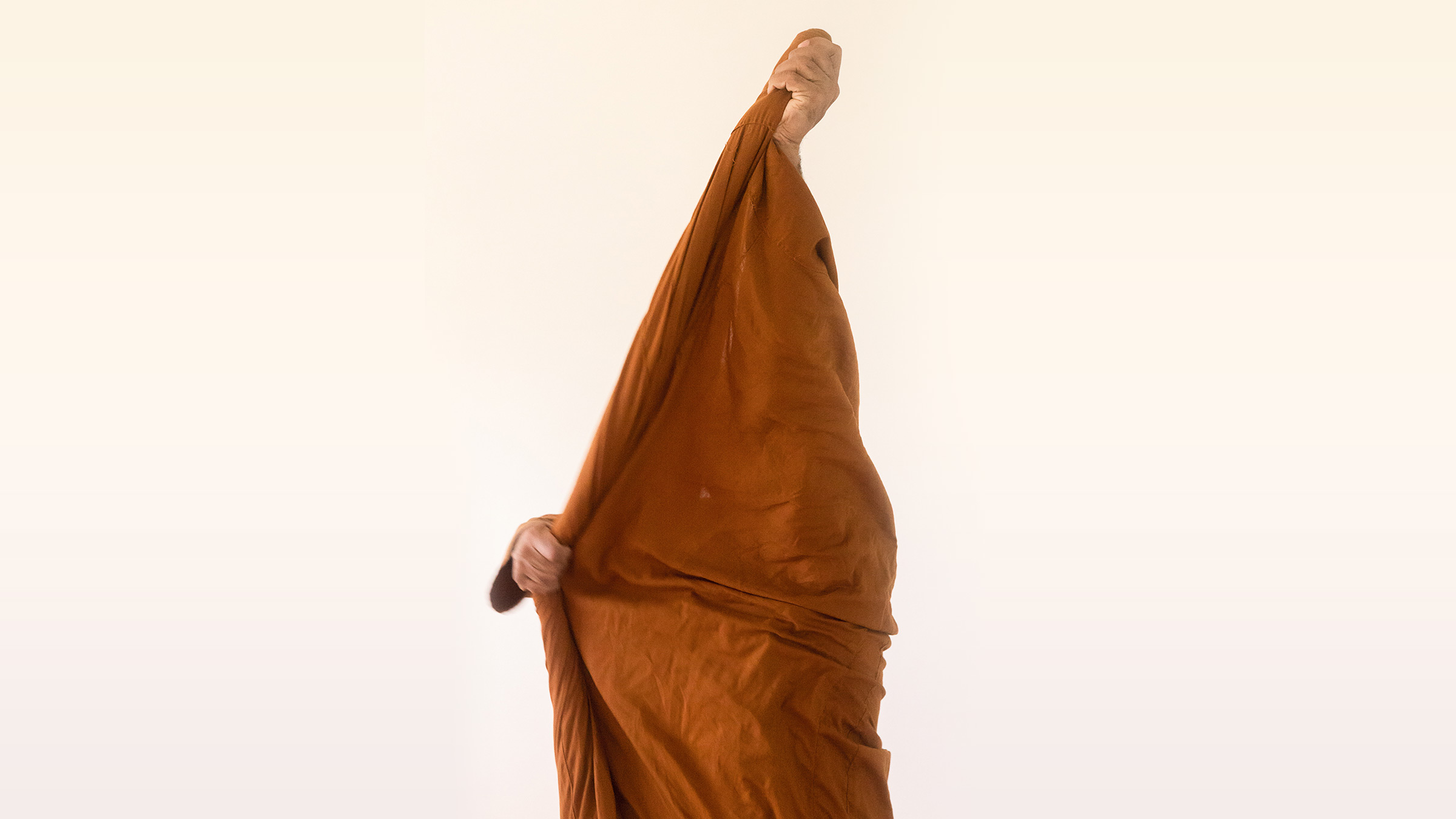 A Buddhist monastic holds up their saffron-colored robe