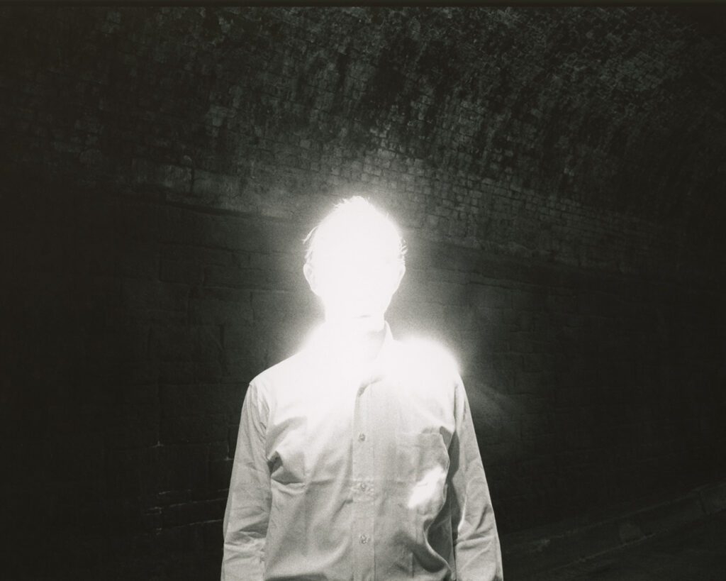 A human figure is depicted wit its facial features obscured by high-exposure light