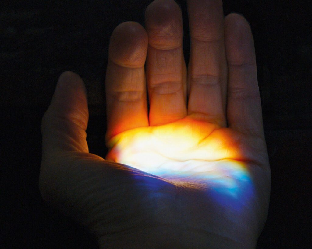 Multicolored light is seen illuminating the palm of an opening hand