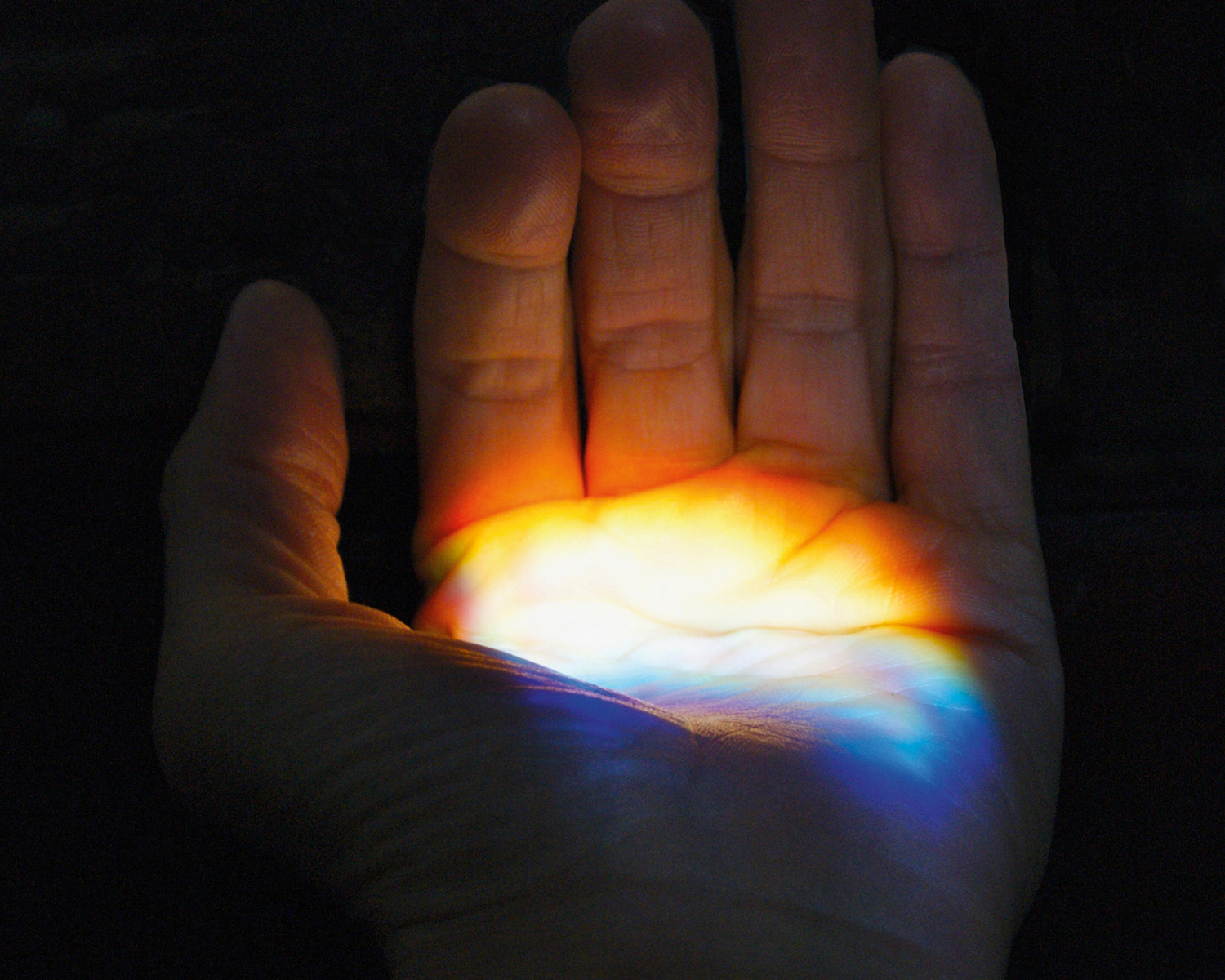 Multicolored light is seen illuminating the palm of an opening hand