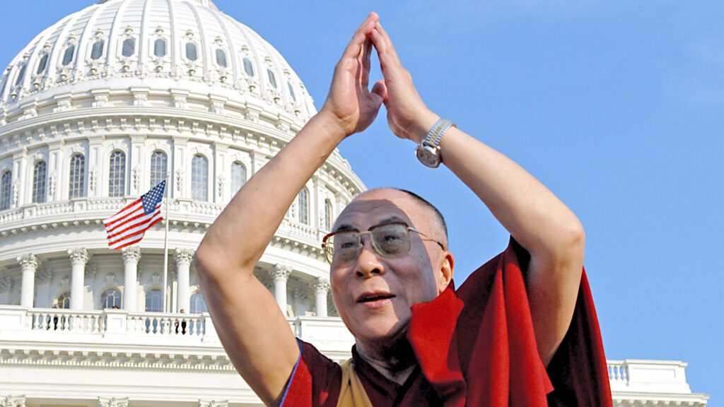 The Dalai Lama, lifting his arms with palms together in front of the US Capitol building.