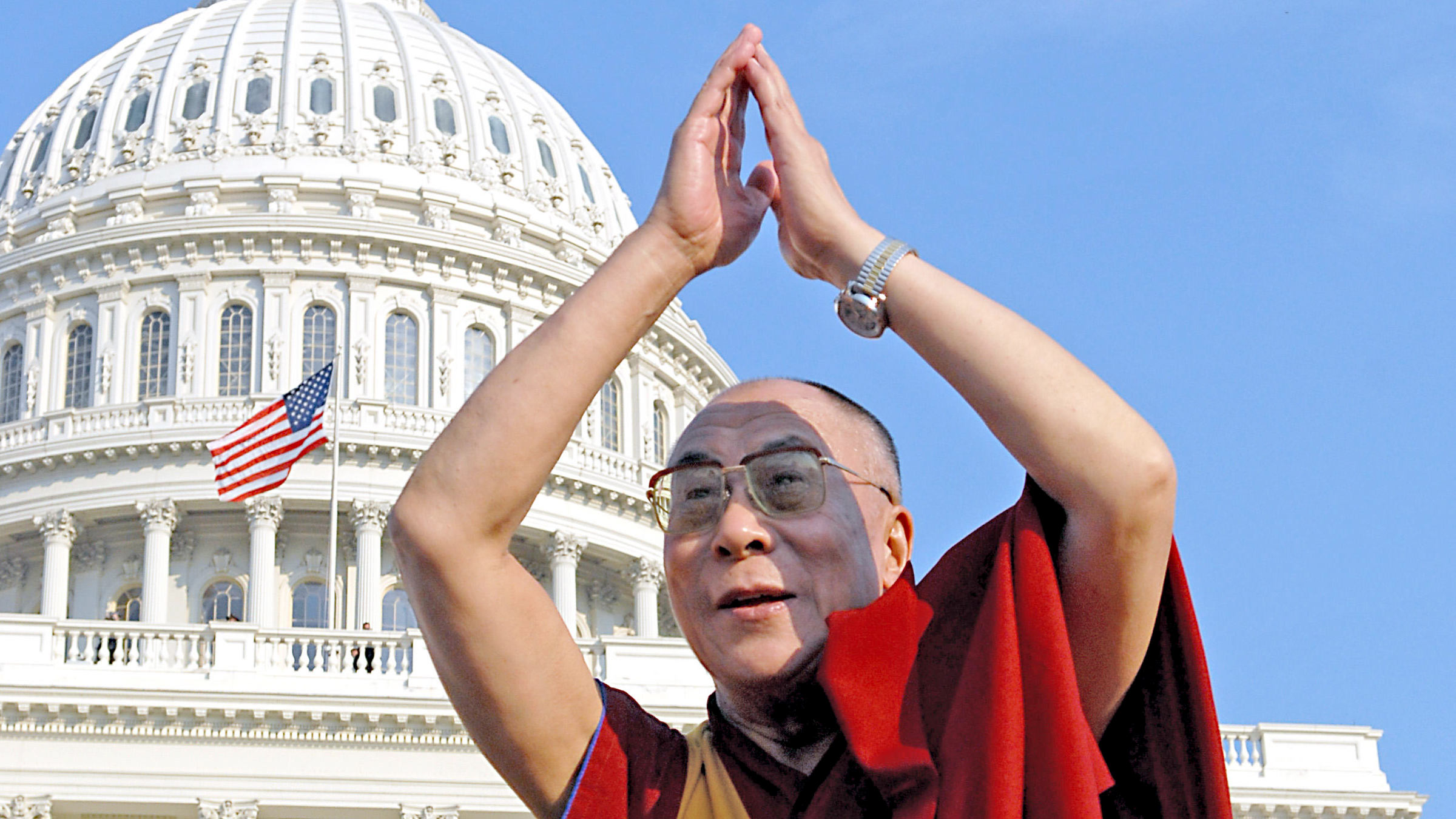 The Dalai Lama, lifting his arms with palms together in front of the US Capitol building.