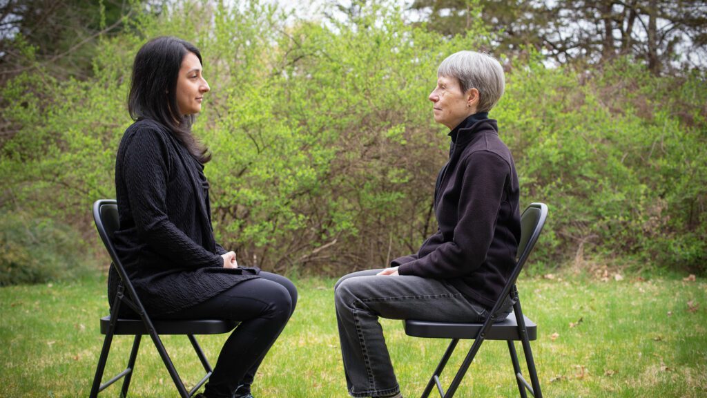 Two people sitting outside on folding chairs facing each other