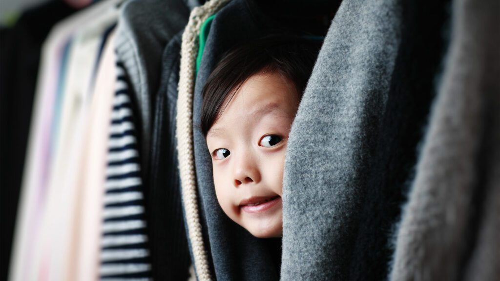 image of a little boy peeping out of hung clothes in closet.