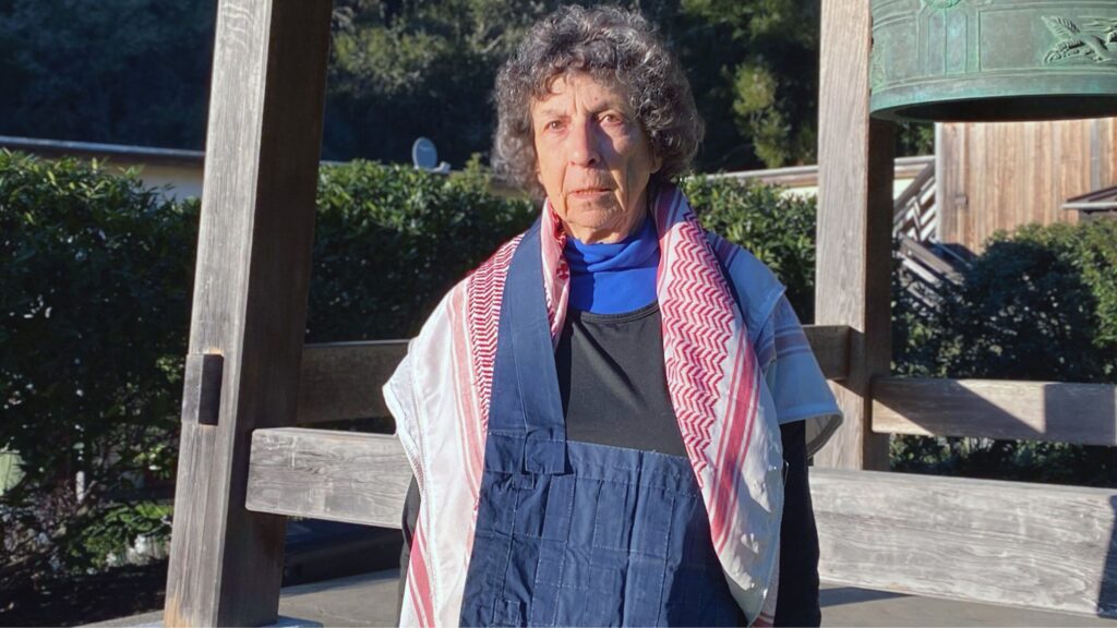 The author, Linda Hess, wears her blue rakusu and red checkered keffiyeh together.