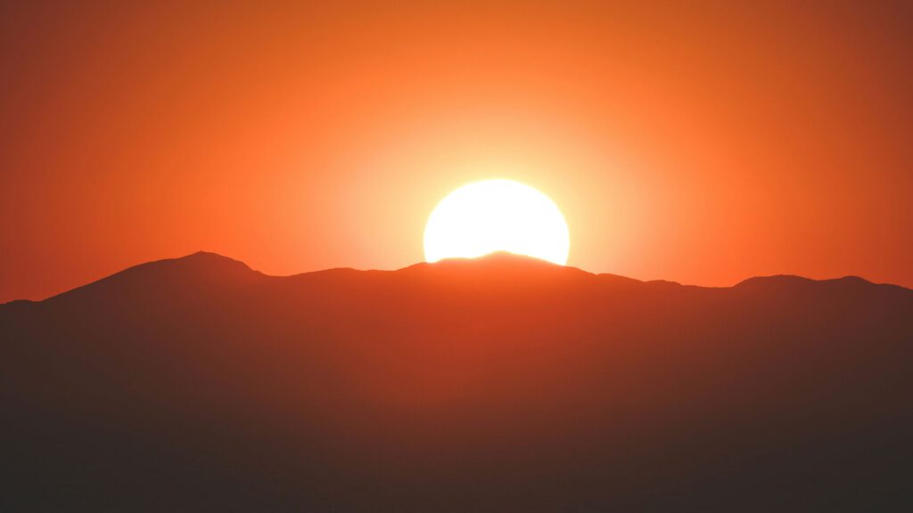 An orange sun rises over a mountain range.