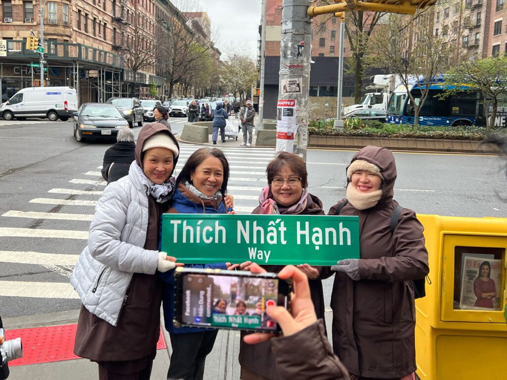 People pose and smile with a street sign that reads "Thich Nhat Hanh Way"