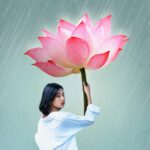 A woman holding a lotus flower as an umbrella.