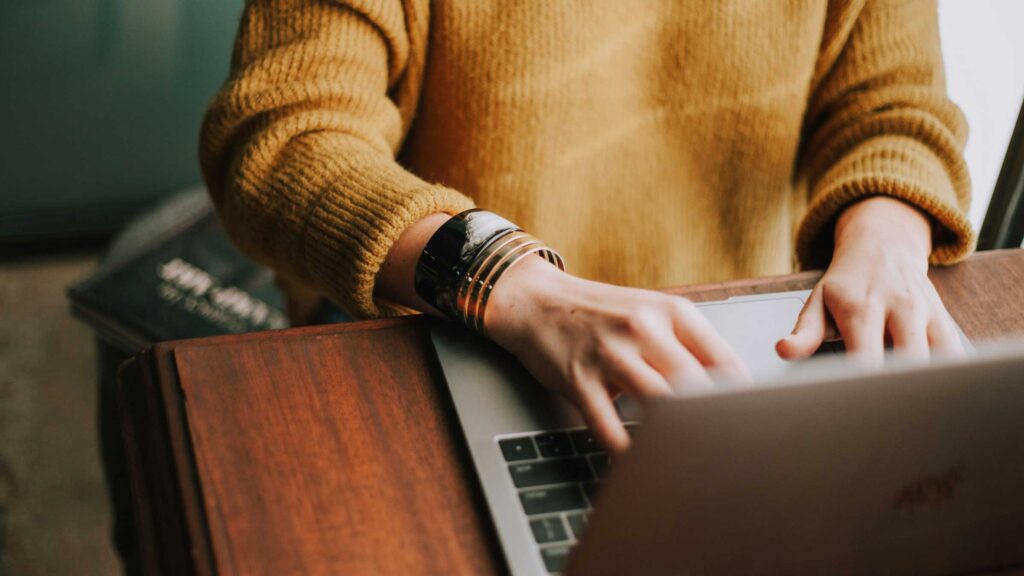 woman in yellow sweater types on a laptop
